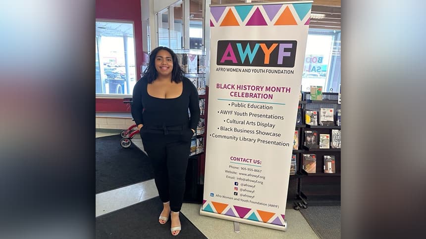 A teenager stands beside a tall sign that says AWYF: Afro Women and Youth Foundation.