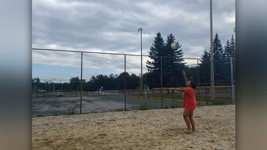 A teenager on a beach volleyball court serving the ball.